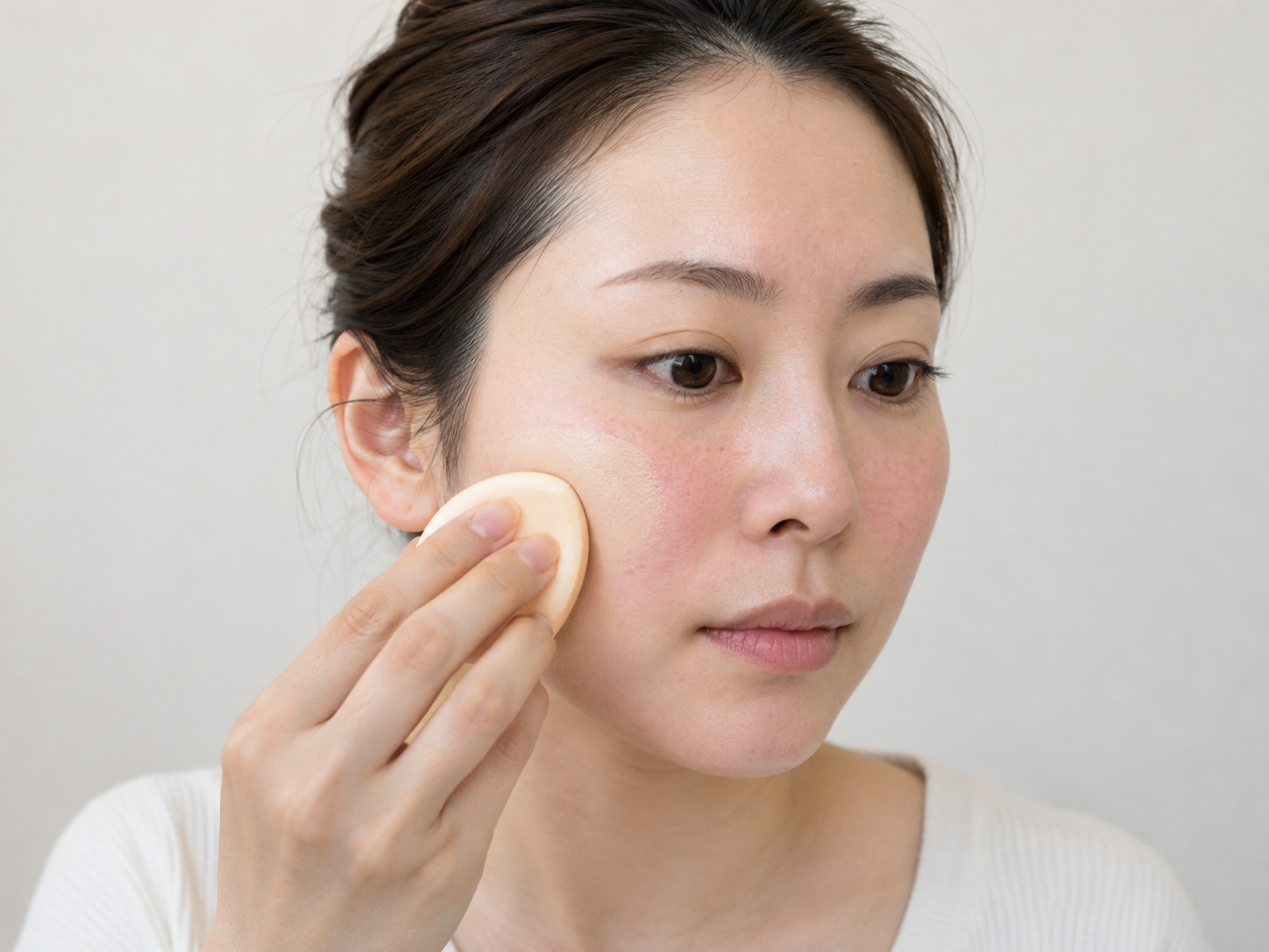 頬の赤みをファンデーションで隠している女性