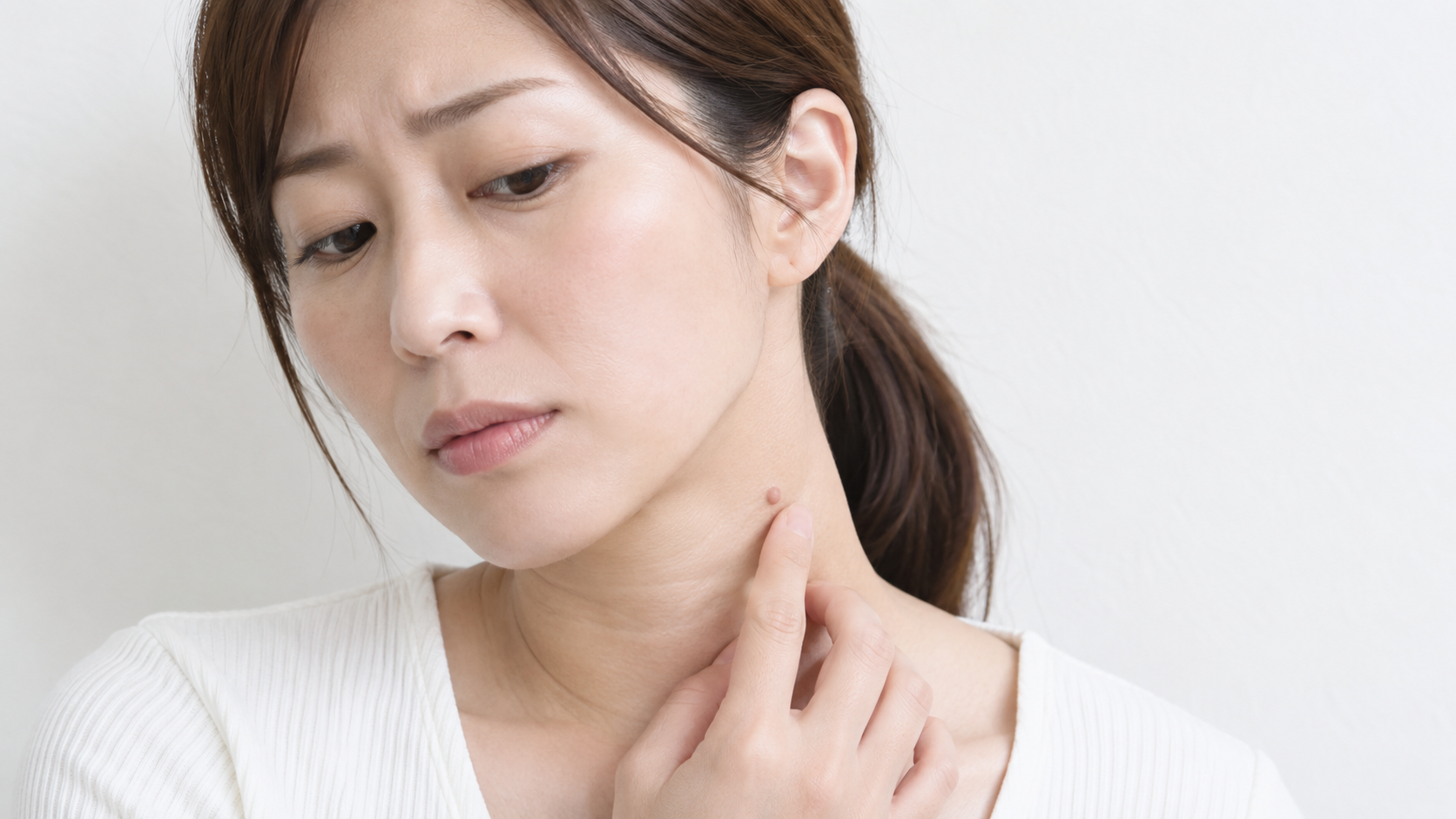 首のイボを気にして触れている女性